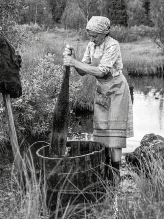 Svartvitt äldre fotografi av en äldre kvinna som tvättar kläder utomhus.